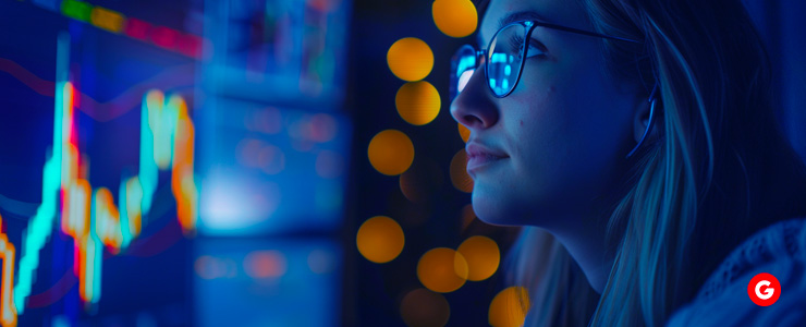 A woman in glasses analyzes a stock chart on a screen, focusing on short selling strategies.