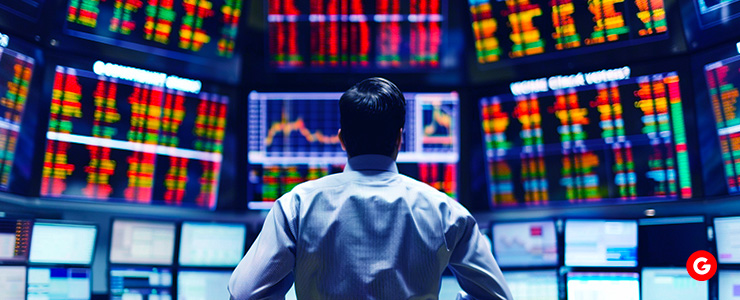 A man in front of a large screen showing various stock market displays.