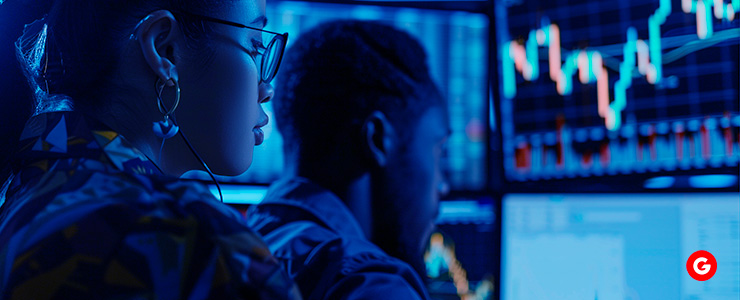 Two individuals analyzing stock market graphs displayed on a computer screen, engaged in a focused discussion.