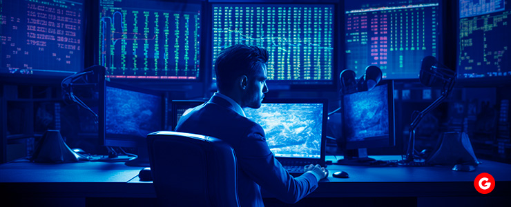 A man seated at a desk, focused on multiple computer screens displaying various data and information.