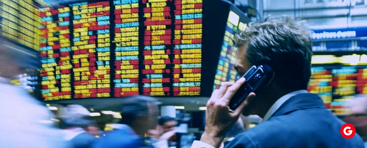 A man speaking on a mobile phone, with a stock market backdrop displaying various stock prices and market activity.